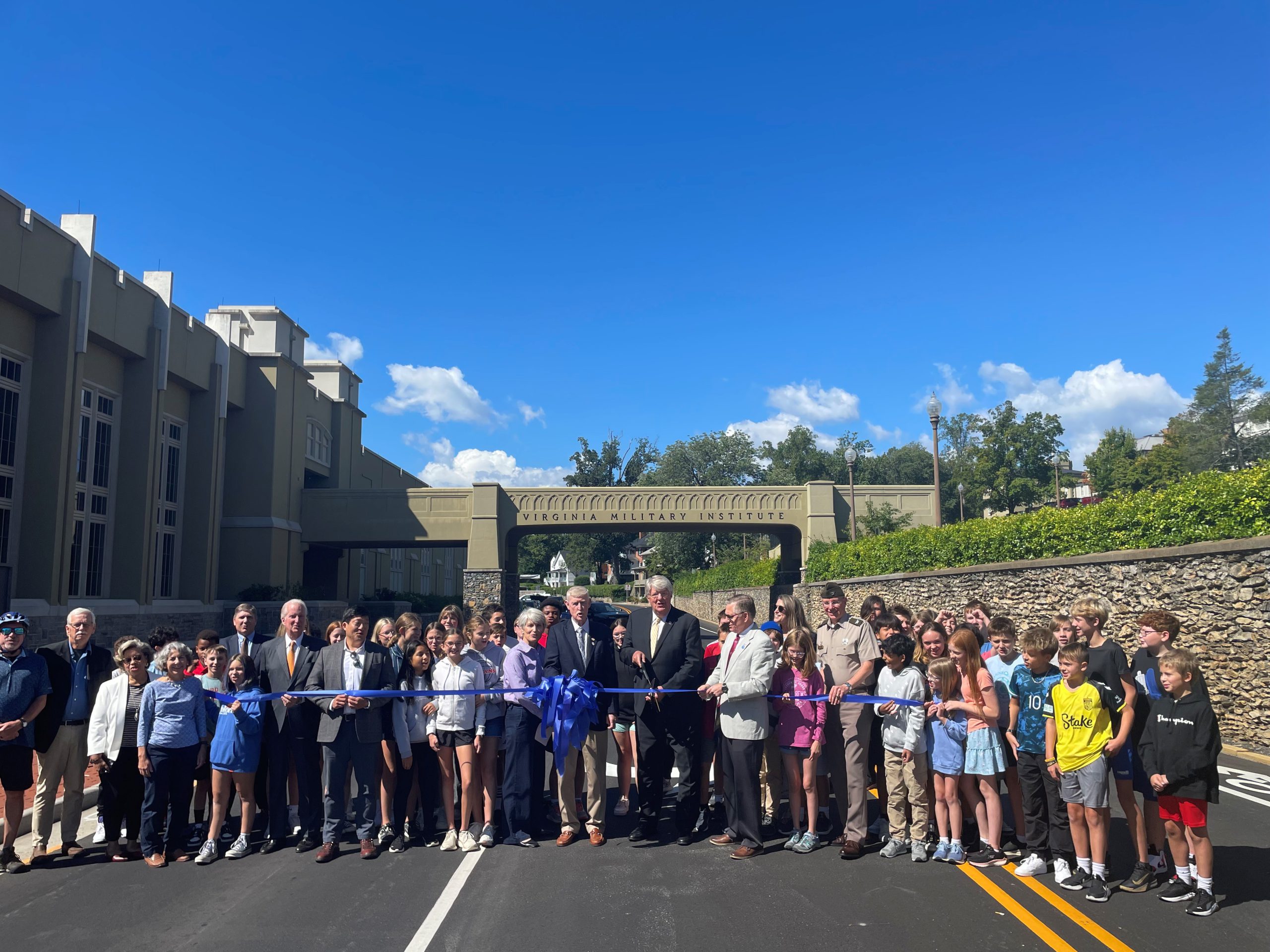 Image of a group of people standing across a road while the Secretary of Transportation cuts a ceremonial ribbon 
